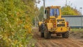 Rural road construction with grader in autumn daytime. The grader repairs the dirt road in the village