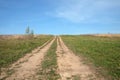 Rural rustic landscape with front view of ground road runs ahead through a green field under clear blue sky to horizon on sunny su Royalty Free Stock Photo