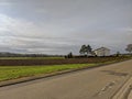 Rural scene with grass, plowed field, and house, near paved road Royalty Free Stock Photo