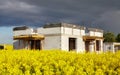 Rural single family house under construction with rapeseed field in foreground and stormy clouds in background