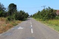 Rural straight paved road between green meadows and trees in summer