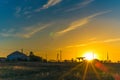 Rural sunset landscape. Sun with rays over the track with wires and silhouettes of buildings and refueling Royalty Free Stock Photo