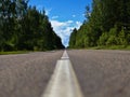 A rural two-lane road, deciduous forest, cloudy sky, highway to the horizon with a bright white dividing strip, horizontal Royalty Free Stock Photo