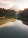 Rural view of lake surrounded by dense of forest with mountain background and blue sky in sunrise time