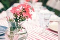Rural wedding table decoration with coral flowers in a glass vase on a striped tablecloth. Special event table set up Royalty Free Stock Photo