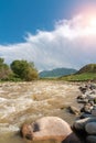 Rushing muddy river under cloudy sky with sunlight Royalty Free Stock Photo