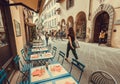Rushing people walk past outdoor restaurant with tables and sets in old city