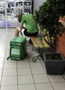 Russia, Chelyabinsk, 08/02/2020 A young Caucasian man, a courier delivering food, sits on a bench resting, next to a large box of Royalty Free Stock Photo