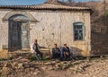 Three senior local men with a cap sitting against the stone house in a rural village of Dagestan