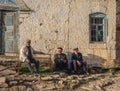 Three senior local men with a cap sitting against the stone wall in a rural village of Dagestan