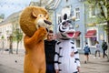 A man in a lion and zebra costume on a city street embraces and takes photos with passers-by. Advertising on the street. Work in