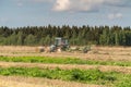 Russia. Gatchinsky district of the Leningrad region. August 28, 2021. The tractor puts hay on the field in the tracks Royalty Free Stock Photo