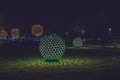 Russia,Krasnodar 07.01.2022. Round glowing balls cast patterned shadows on a lawn surrounded by glowing trees in a dark