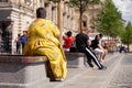 Russia Moscow 2019-06-17 Back view of fat woman in yellow dress sitting on bench, looking at St. Basil's Cathedral. People walk o