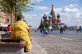 Russia Moscow 2019-06-17 Back view of fat woman in yellow dress sitting on bench, looking at St. Basil's Cathedral. People walk o