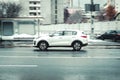 Fast moving Kia Sportage SUV rides on a wet city street. White crossover car on slippery road in motion. Overspeed in city concept