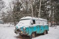 An old rusty ambulance van stands in a snow-covered clearing on a cloudy winter day.