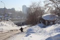 A woman walks on an inclined road in winter in the city past wooden houses in an alley