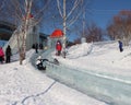 funny people and children ride from a high ice slide in the park in winter entertainment from a