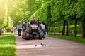 Russia, Peterhof, 16.06.2022 - A team of gardeners rides on a garden tractor in a large park.