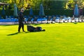 A man with a lawn mower mows grass on the lawn at a country club by the pool. Royalty Free Stock Photo