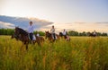 Girls in white shirts are riding horses on a blooming meadow in the rays of the setting sun.