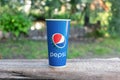 08/05/2020 Russia. Saint Petersburg. A disposable glass with the Pepsi Cola logo stands on a wooden tabletop, on a summer green ba