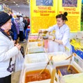 a young saleswoman selling Siberian honey at the city fair. Text in Russian: Taiga honey, with cedar grease