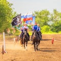 Russian young Cossacks gallop with banners on horses in summer sunny day.