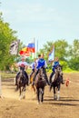 Russian young Cossacks gallop with banners on horses in summer sunny day.