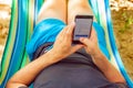 A young man lies on a hammock and looks at a smartphone on a summer sunny day