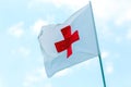 Flag with a red cross develops against a blue sky. Red Cross emblem of the international Red Cross, international humanitarian org Royalty Free Stock Photo
