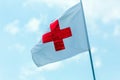 Flag with a red cross develops against a blue sky. Red Cross emblem of the international Red Cross, international humanitarian org Royalty Free Stock Photo