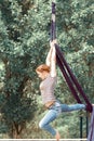 A young woman performs gymnastic exercises on ropes in a city park
