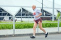 An elderly man runs a long distance against the background of the stadium