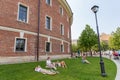 Russia, St. Petersburg. 07/24/2021. People girls guys are resting on the grass near a brick window with large windows, a city summ