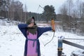 A girl shoots in the winter from a bow at the festival of medieval Vikings