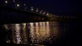 Russian city road bridge across the river. The night bridge glows with lanterns and reflects glare on the water Royalty Free Stock Photo