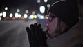 Russian girl freezes in the cold. A woman in gloves in winter rubs her palms and blows warm air from her mouth to keep warm