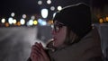 Russian girl freezes in the cold. A woman without gloves in winter rubs her palms and blows warm air out of her mouth to keep warm