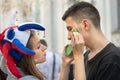 Russian girl sport fan in a colorful hat drawing brazilian flag on the cheek of brazilian man Royalty Free Stock Photo