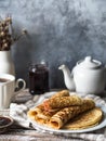 Russian homemade yeast pancakes rolled into a tube on white plate, jam and tea in the mug on wooden table. Traditional wheat