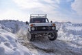 Russian offroad SUV `Lada Niva 4x4` quickly with splashes of snowstorm rides through the snow in winter with a cheerful driver in