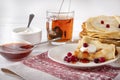 Pancakes with berries and sour cream on a plate, tea, jam on a towel with a red pattern on a white background Royalty Free Stock Photo