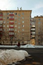 Russian panel house and windows of different apartments with red balconies. Winter landscape. Pile of snow