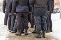 Russian police officers legs in black ankle boots, red stripe pants and with rubber tonfa night sticks.