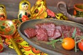 Russian salami sausages sliced on rustic wooden plate, bright matroshka dolls, spoon khokhloma Royalty Free Stock Photo