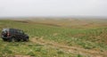 Russian SUV UAZ Patriot on a hillside in the piedmonts in Uzbekistan, Central Asia, view of the plain, gray cloudy sky