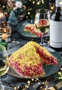 Russian Traditional New Year salad herring under fur coat - shuba in plate on dark table served with glasses, bottle of wine,