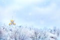 Russian winter landscape. Golden domes of the church against the background of a winter white forest. Snowing.